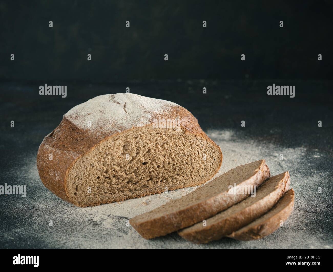 Fette di pasta madre casalinga pane di segale con la farina di segale sul nero testurizzato sfondo. Copia dello spazio. Tasto basso Foto Stock