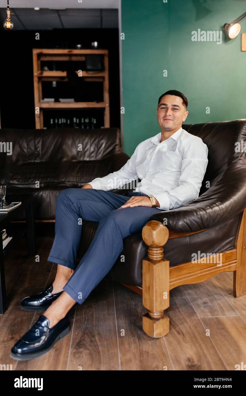 Uomo sorridente nella camicia da donna seduta sulla poltrona Foto Stock