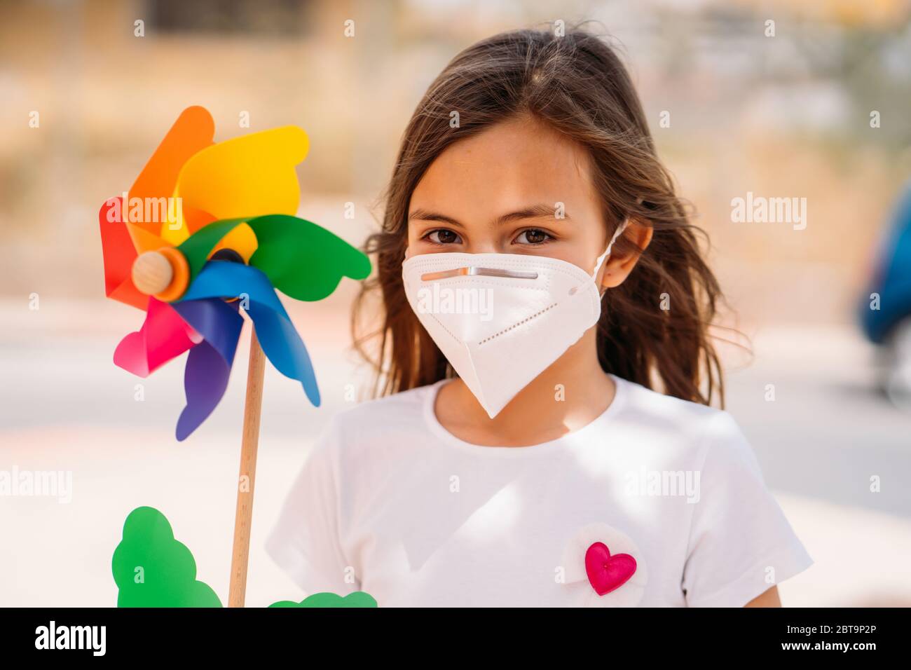 Bambina che indossa la maschera e tiene un colorato mulino a vento giocattolo, o pinwheel. Foto Stock