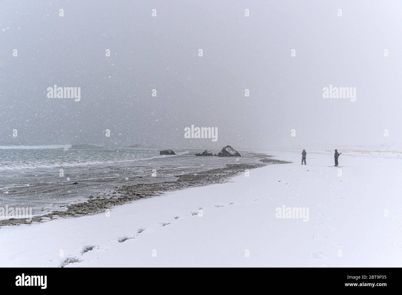 Persona irriconoscibile fotografare una roccia sulla spiaggia durante una tempesta di neve ventosa Foto Stock