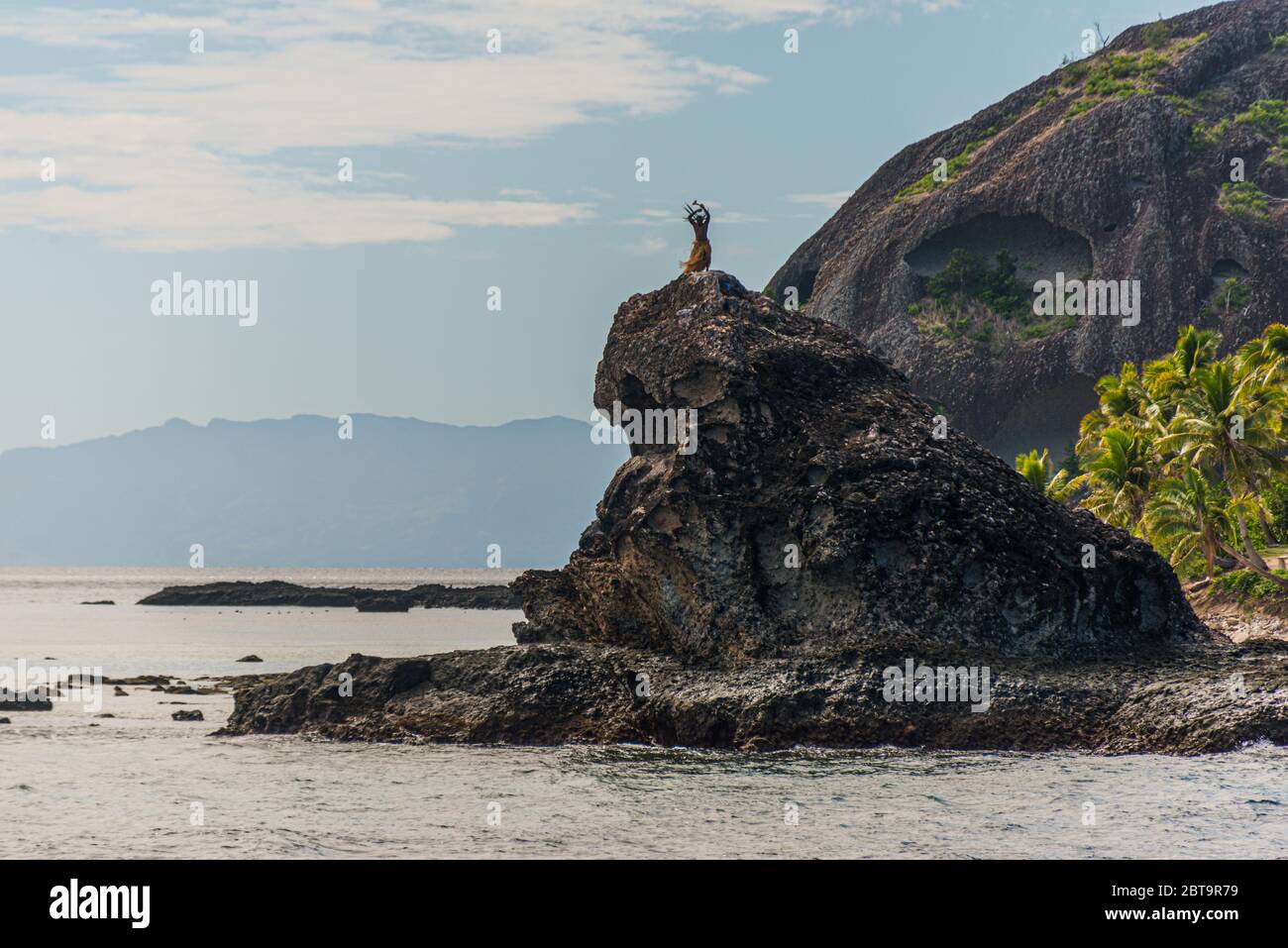 Abitanti dell'isola delle Fiji che ballano su una roccia nel mare, vicino ad un'isola tropicale. Isole Yasawa, Figi Foto Stock