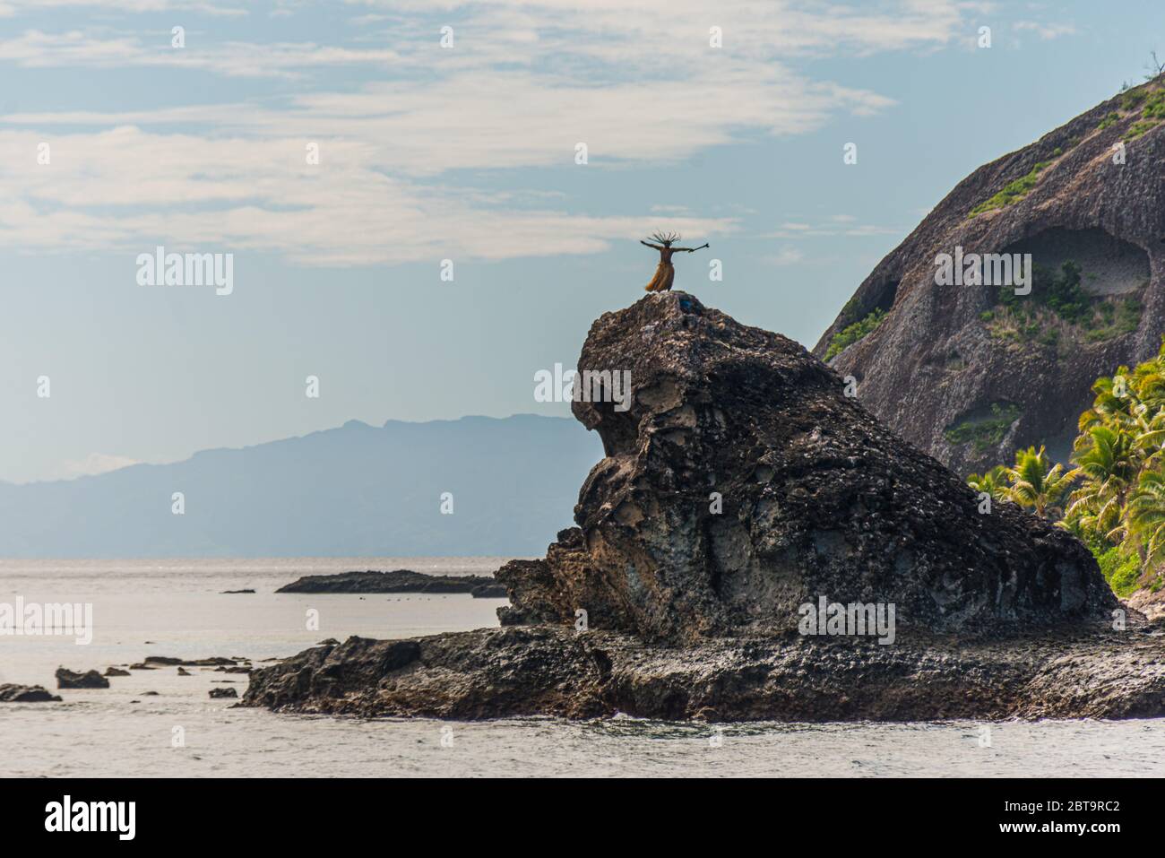Abitanti dell'isola delle Fiji che ballano su una roccia nel mare, vicino ad un'isola tropicale. Isole Yasawa, Figi Foto Stock