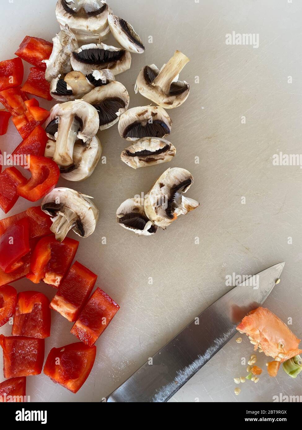 Peperoni rossi e funghi tagliati sulla scrivania in una cucina Foto Stock