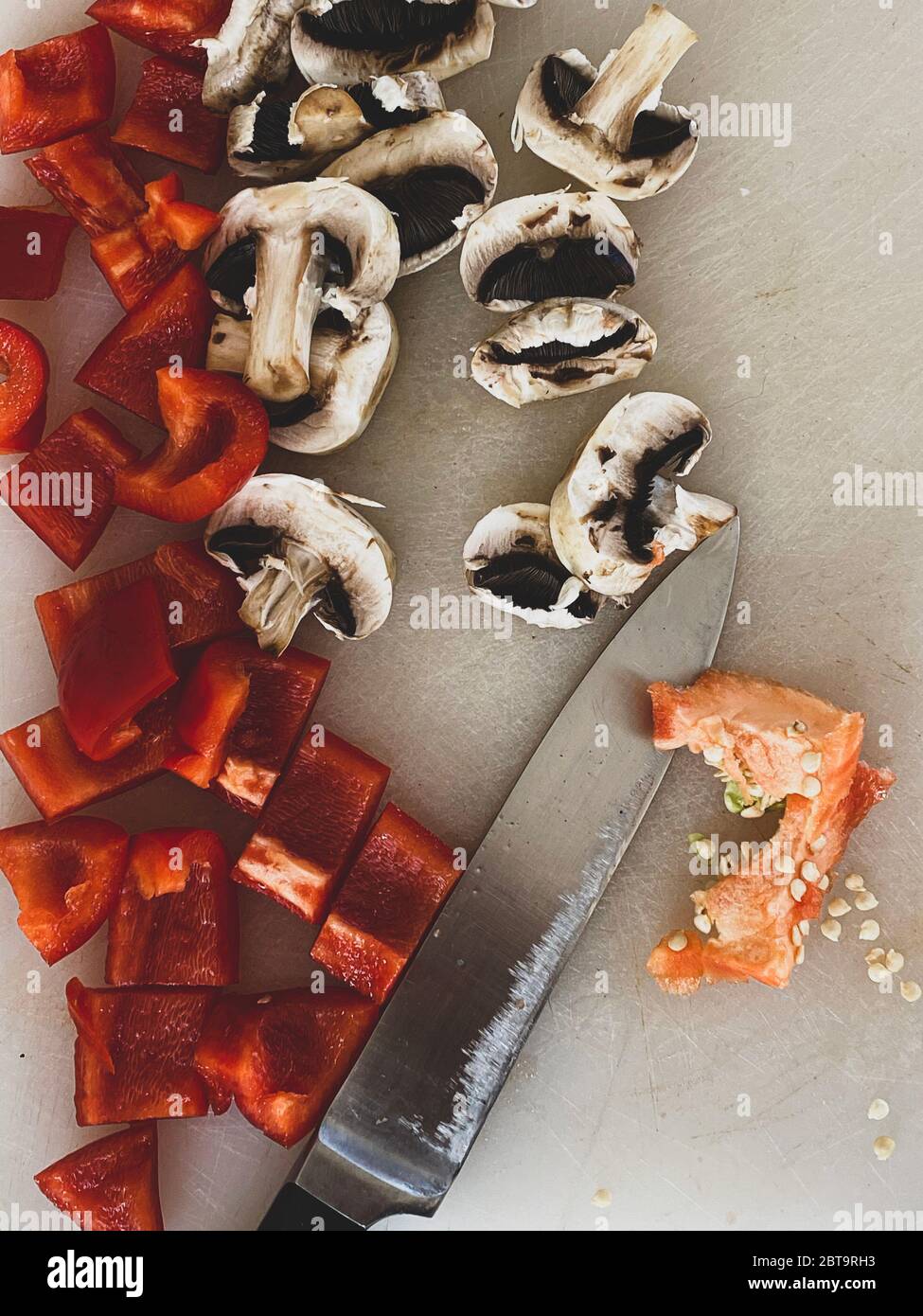 Peperoni rossi e funghi tagliati sulla scrivania in una cucina Foto Stock