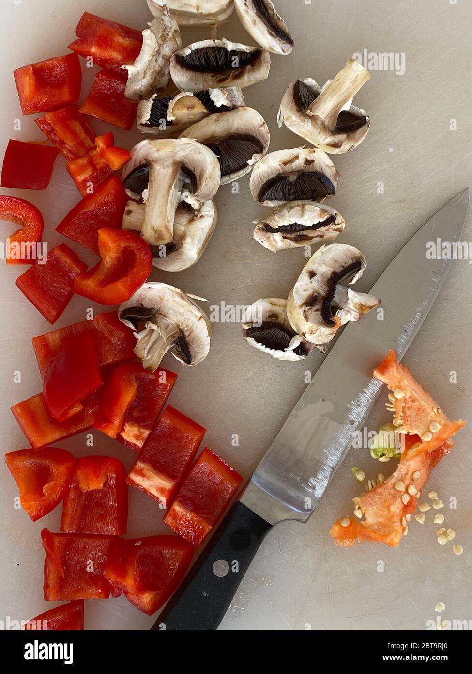 Peperoni rossi e funghi tagliati sulla scrivania in una cucina Foto Stock