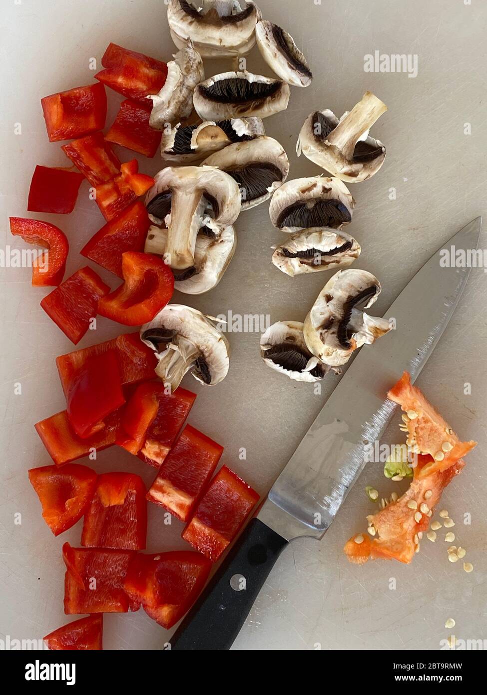 Peperoni rossi e funghi tagliati sulla scrivania in una cucina Foto Stock