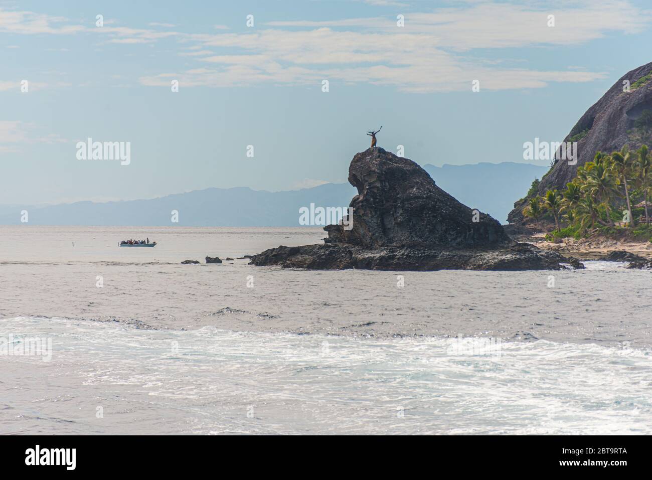 Abitanti dell'isola delle Fiji che ballano su una roccia nel mare, vicino ad un'isola tropicale. Isole Yasawa, Figi Foto Stock