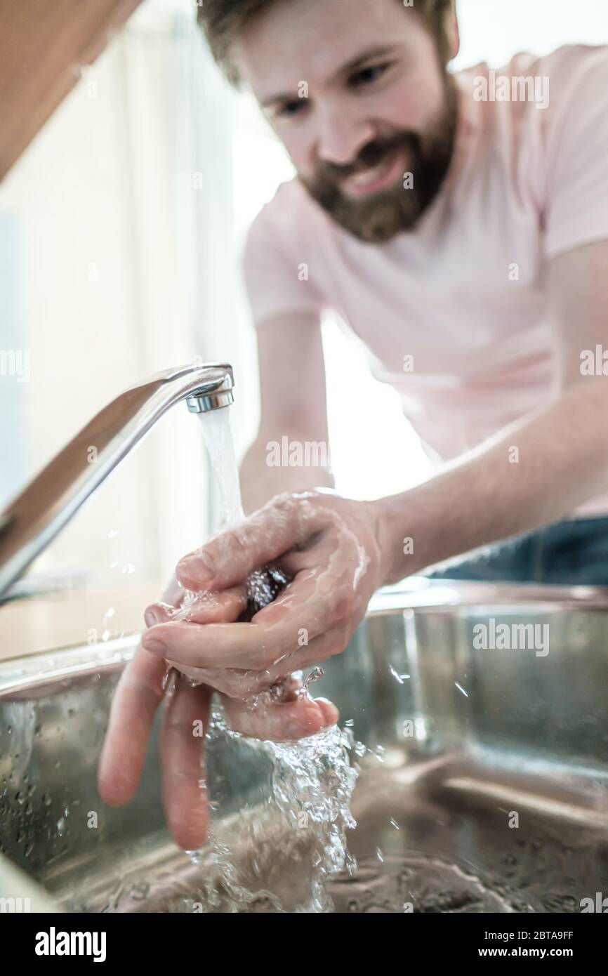 Mani sotto un flusso di acqua pulita, su uno sfondo sfocato, un uomo sorridente osservando le regole dell'igiene. Concetto di salute. Foto Stock