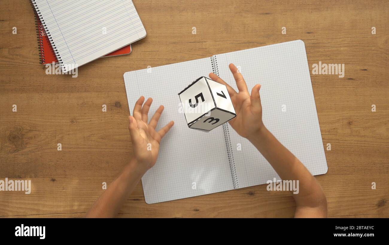 Bambino seduto al tavolo con i quaderni e giocando con i dadi di carta. Vista dall'alto Foto Stock