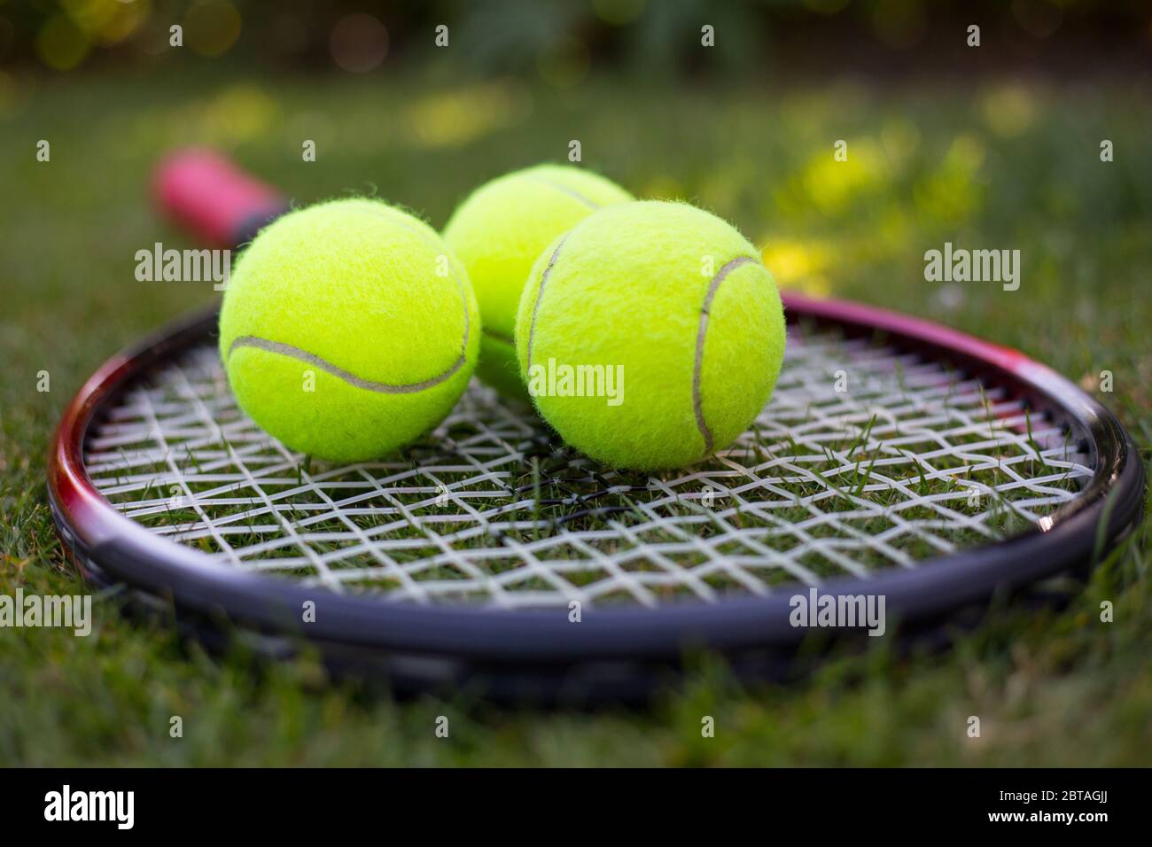 Una racchetta da tennis e tre palle da tennis gialle sull'erba Foto Stock