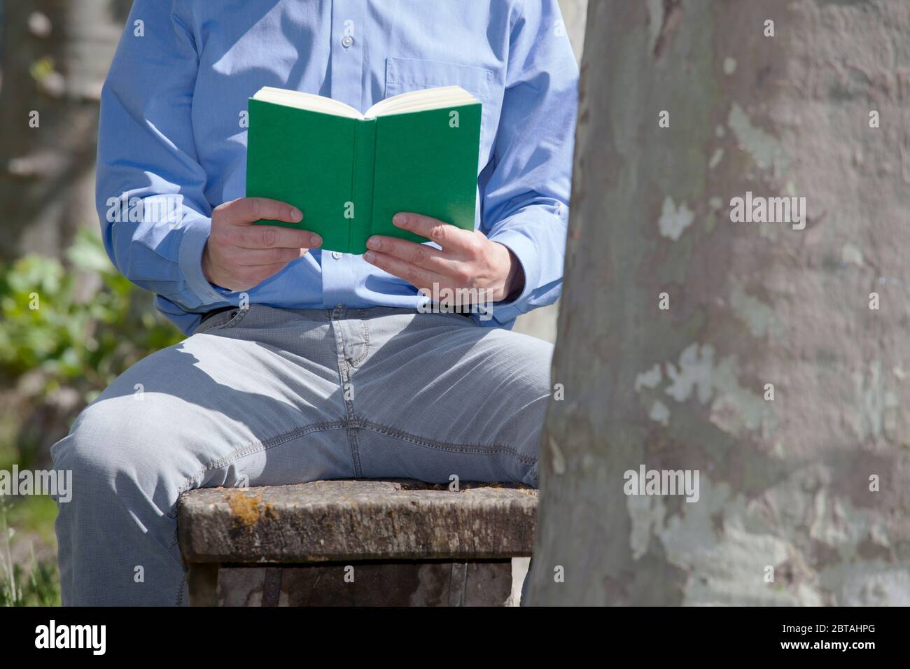 Uomo d'affari seduto su una panchina in un parco che legge un libro verde - fuoco sul libro Foto Stock