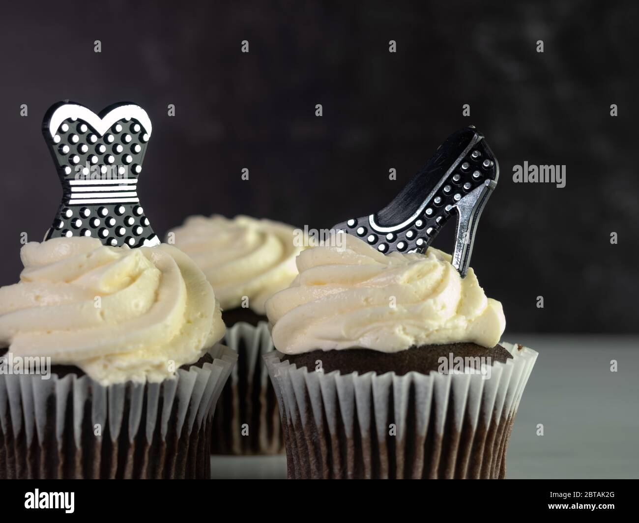 Cupcake al cioccolato con glassa bianca e swirled decorata con un abito a pois nero e argento e scarpe alte tacco perfetto per il pelo, il matrimonio, o. Foto Stock