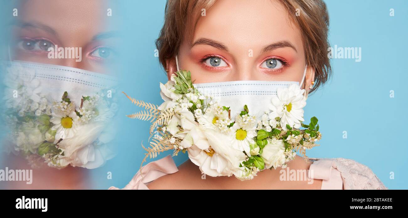 Maschera viso con fiori. Ritratto di bella donna con occhi blu, make-up moda e maschera su parete blu Foto Stock