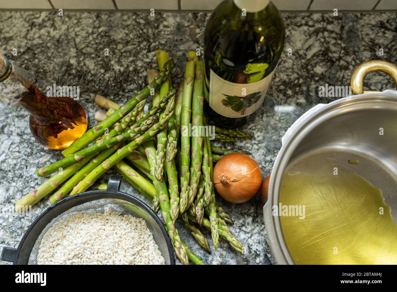 Cucinando del riso risotto con asparagi, cipolla e vino bianco. Padella con olio d'oliva su fondo di granito. Vista ad angolo alto. Foto Stock