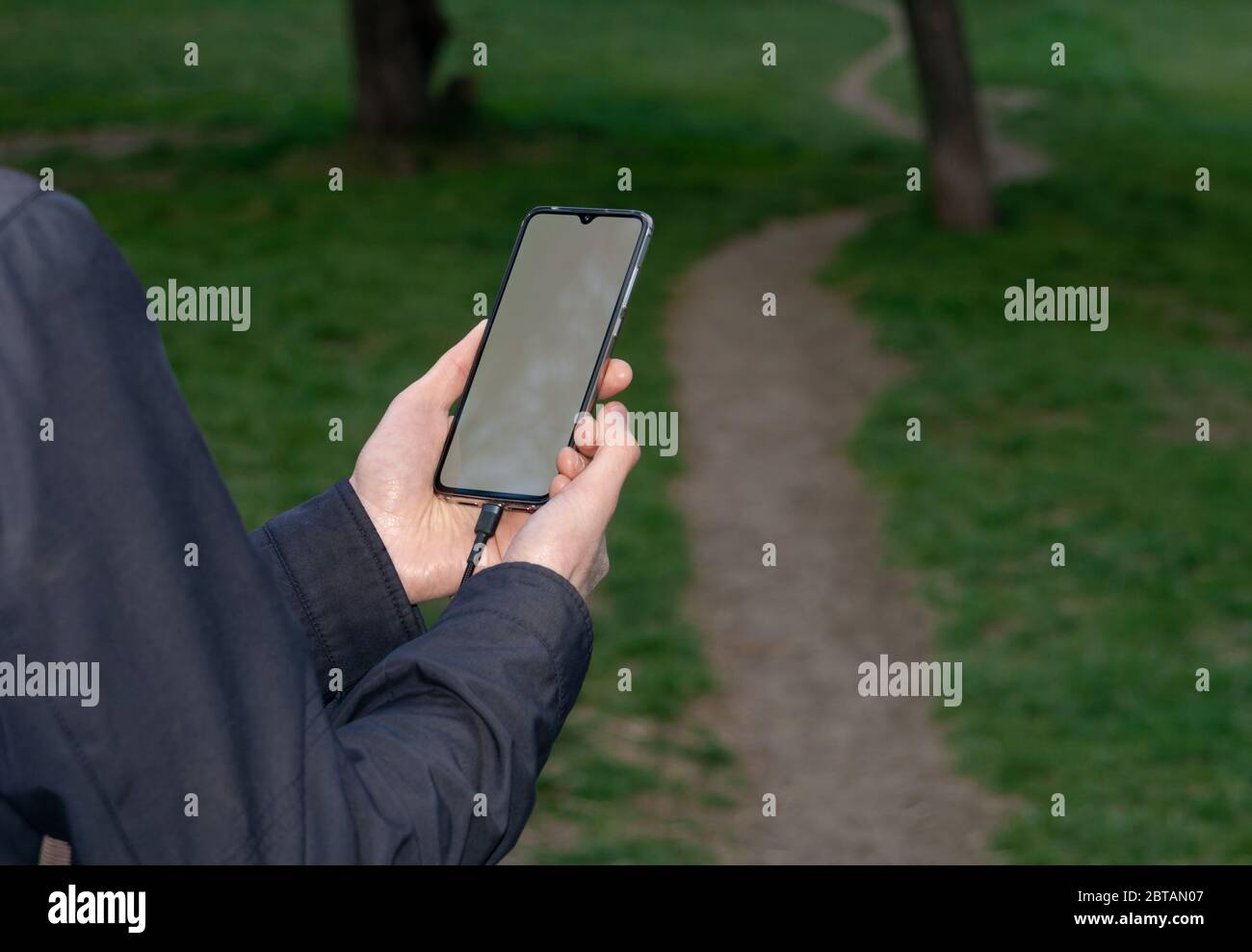 Un uomo usa uno smartphone mentre cammina sul sentiero alla natura. Concetto di tecnologia moderna. Messa a fuoco selettiva Foto Stock