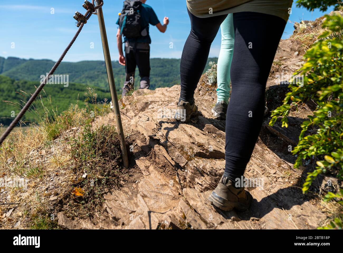 Una donna che cammina un sentiero attraverso i vigneti su una superficie rocciosa, ardesia in scarpe da arrampicata specializzate da una ringhiera metallica, sullo sfondo si erge un m Foto Stock