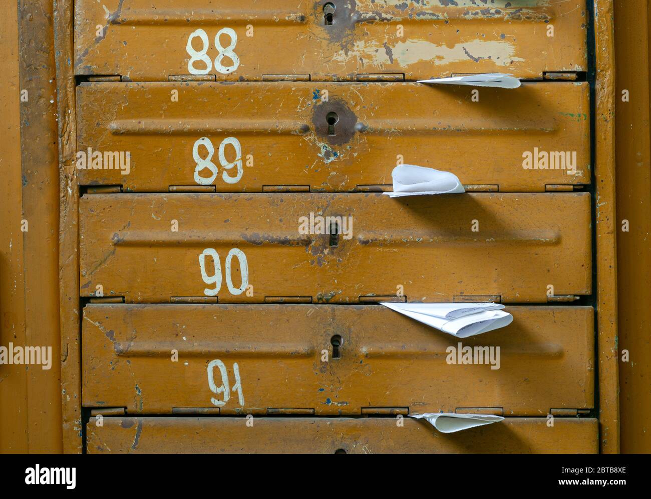 Vecchie caselle postali nella sala d'ingresso di una casa residenziale piena di volantini di carta bianca. Concetto di mailing di massa Foto Stock