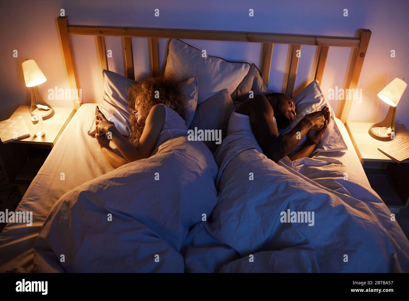 Sopra il ritratto di giovane coppia mista-corsa sdraiata indietro a letto e utilizzando smartphone, copia spazio Foto Stock