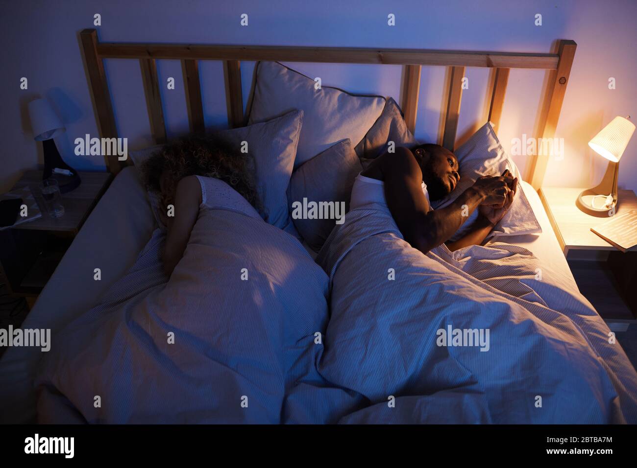 Sopra la vista ritratto di afroamericano uomo utilizzando smartphone a letto di notte mentre si trova accanto a moglie o ragazza, spazio copia Foto Stock