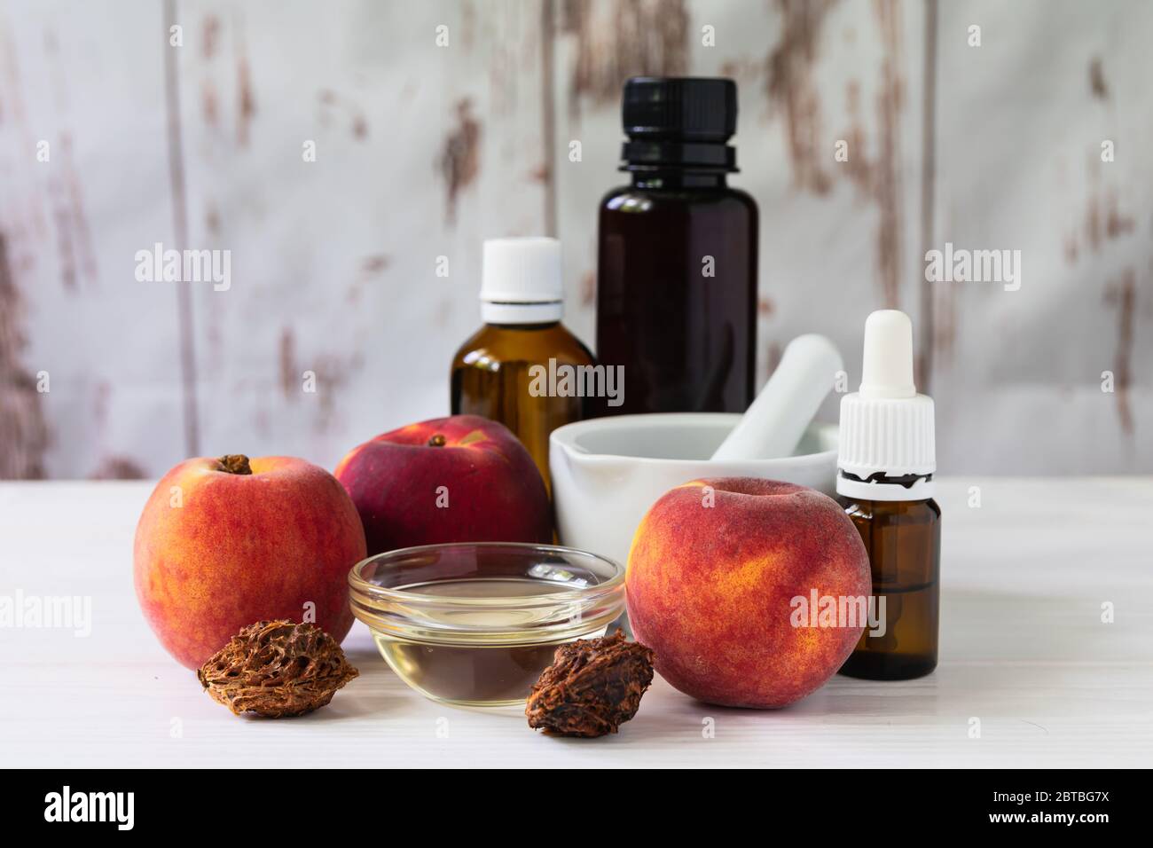 concetto cosmetico naturale, pesche con bottiglie di vetro con olio e malta, su fondo bianco di legno Foto Stock