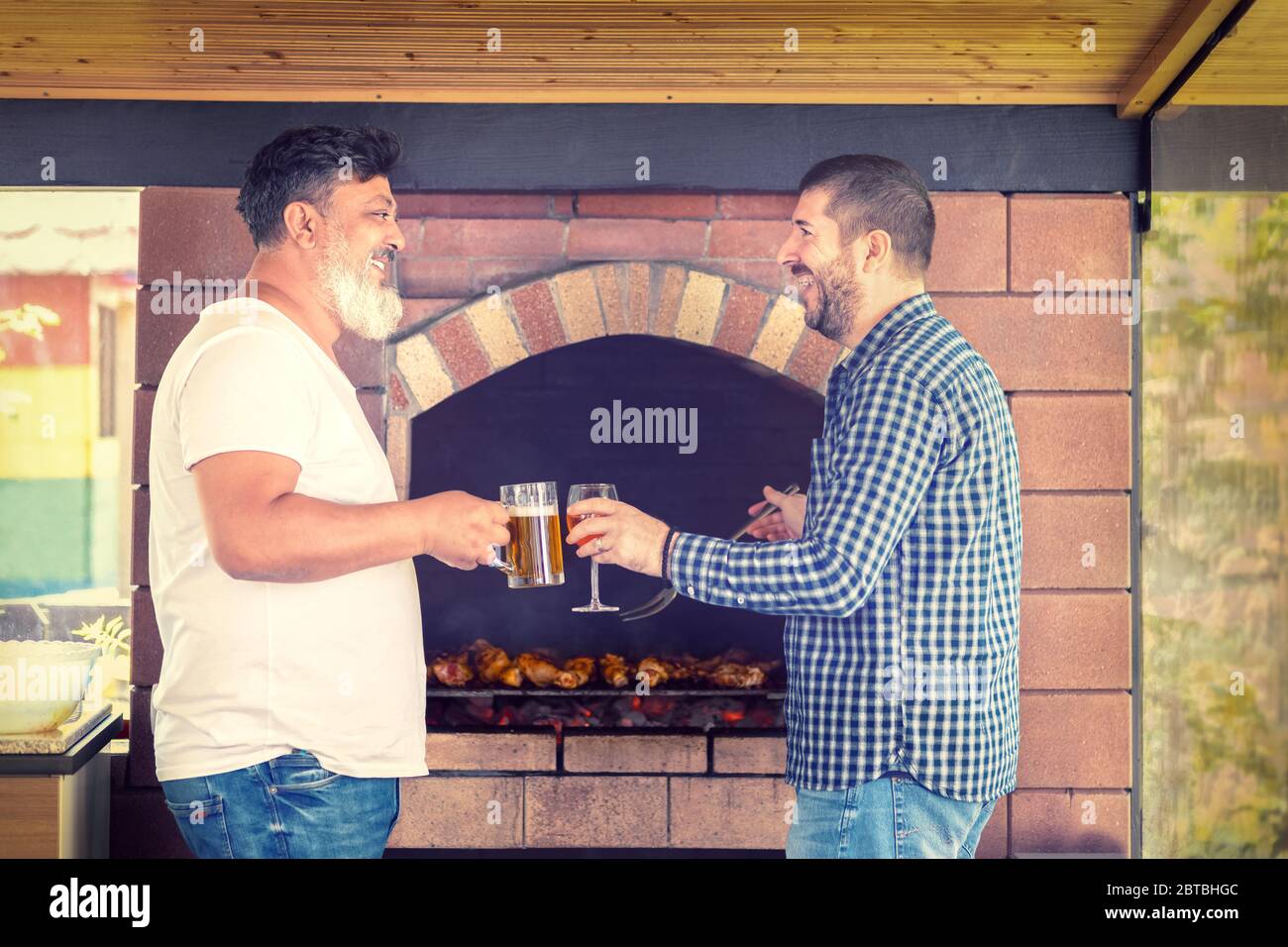 Amici maschi multirazziali che si divertono a cucinare carne alla griglia barbecue mentre bevono alcol Foto Stock