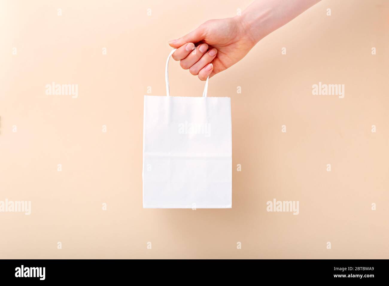 Borsa per la spesa in carta bianca in mano femminile su sfondo beige di colore chiaro. Consegna, shopping, vendita concetto regalo. Pacchetti di borse per mockup. Spazio per la copia Foto Stock
