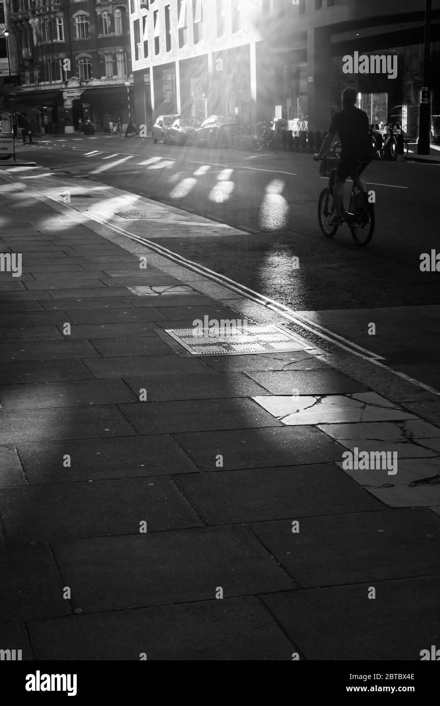 Scena stradale bianca e nera con singolo ciclista che passa sotto il sole Foto Stock