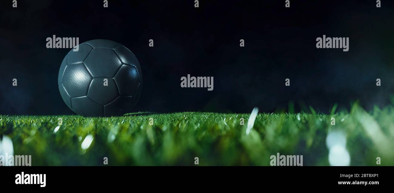 Angolo basso primo piano di una palla di calcio nera sull'erba verde del campo da calcio su sfondo scuro per lo spazio di copia Foto Stock