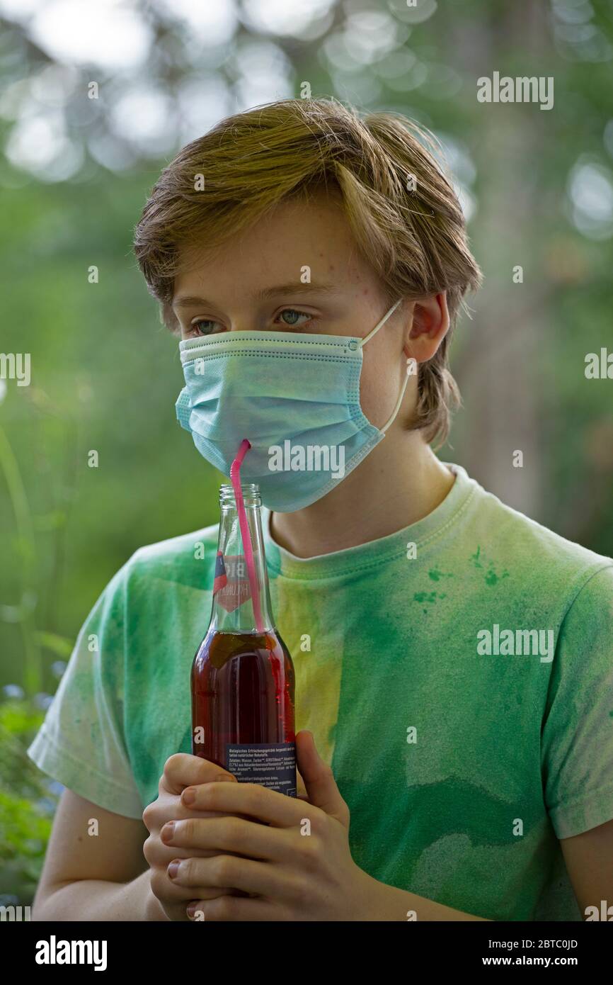 Ragazzo che indossa una maschera di respirazione che beve da una bottiglia usando una paglia, Germania Foto Stock