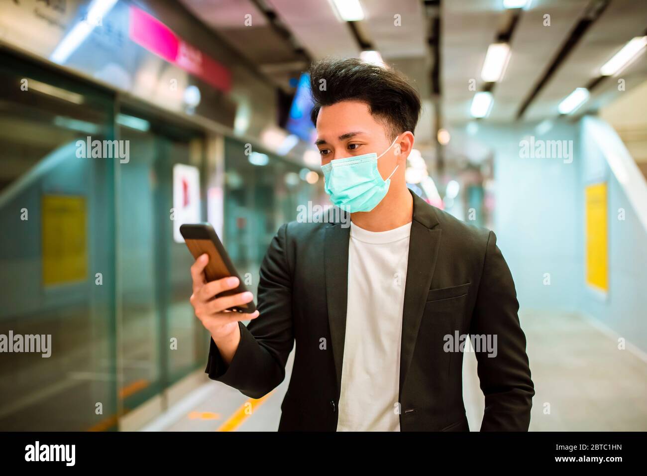 giovane uomo d'affari che indossa la maschera di visione del telefono cellulare e in attesa del treno Foto Stock