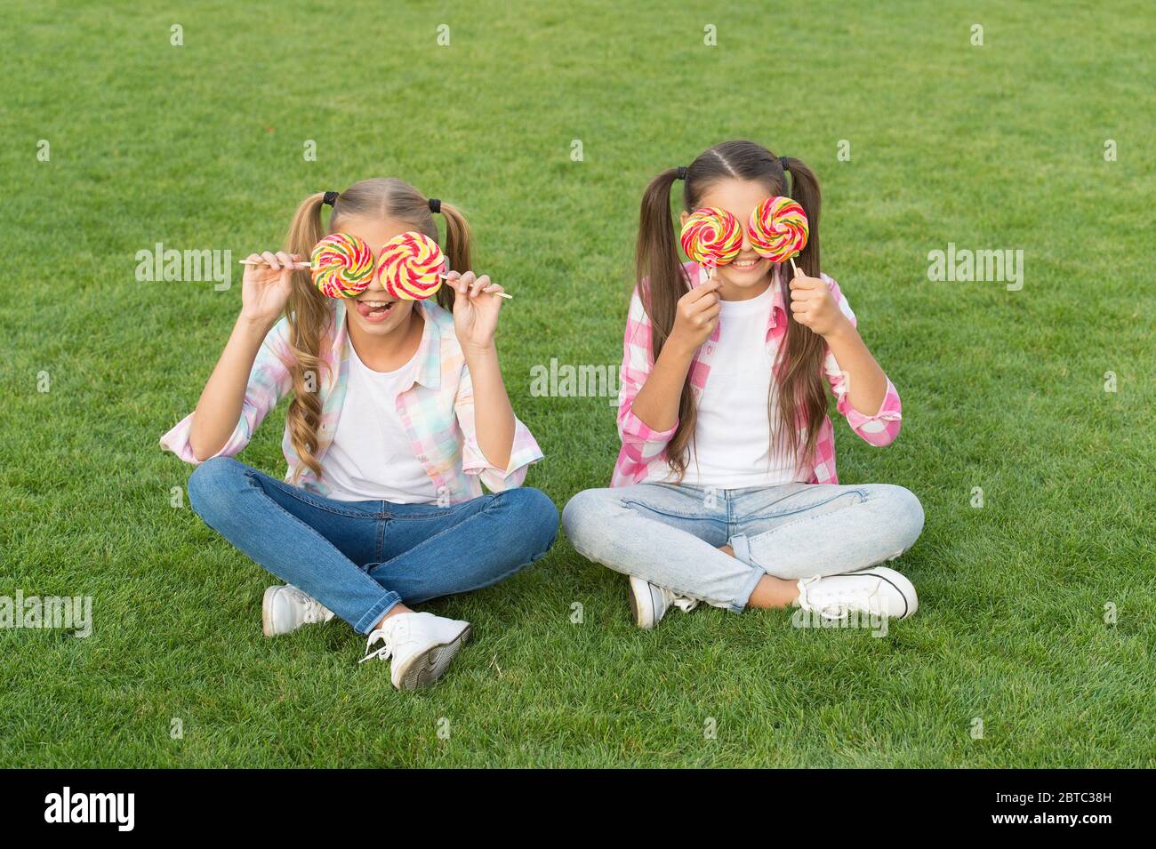 Non solo dolce ma meraviglioso da guardare. Bambine con dolce sguardo su  erba verde. I bambini felici coprono gli occhi con le caramelle. Dolci.  Negozio di caramelle. Pasticceria a base di zucchero.