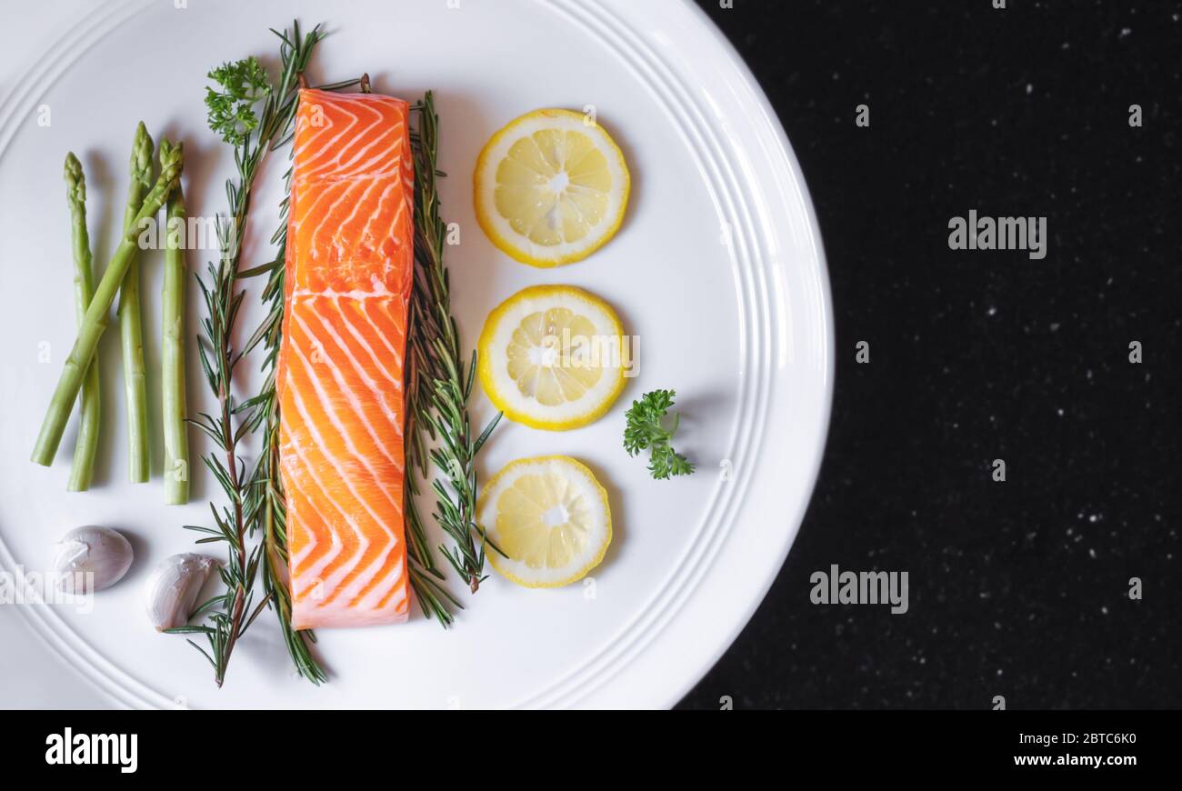 Filetto di salmone fresco crudo con erbe e ingredienti, su piatto bianco Foto Stock
