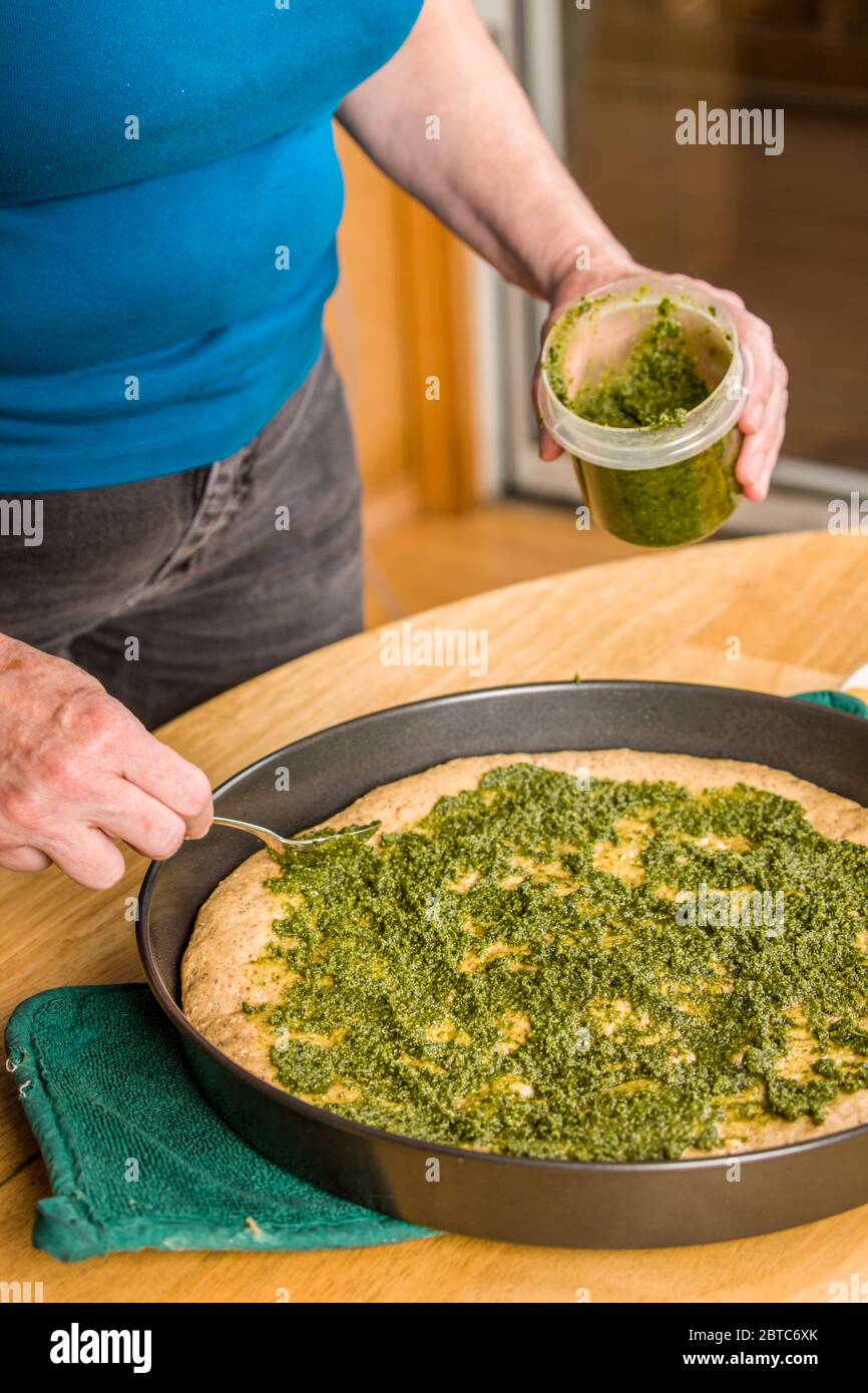 Versare la salsa al pesto sulla crosta a grani multipli parzialmente cotta prima di aggiungere altre condimenti. Foto Stock