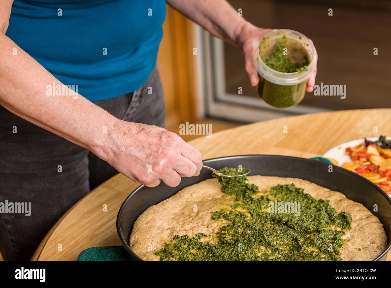Versare la salsa al pesto sulla crosta a grani multipli parzialmente cotta prima di aggiungere altre condimenti. Foto Stock