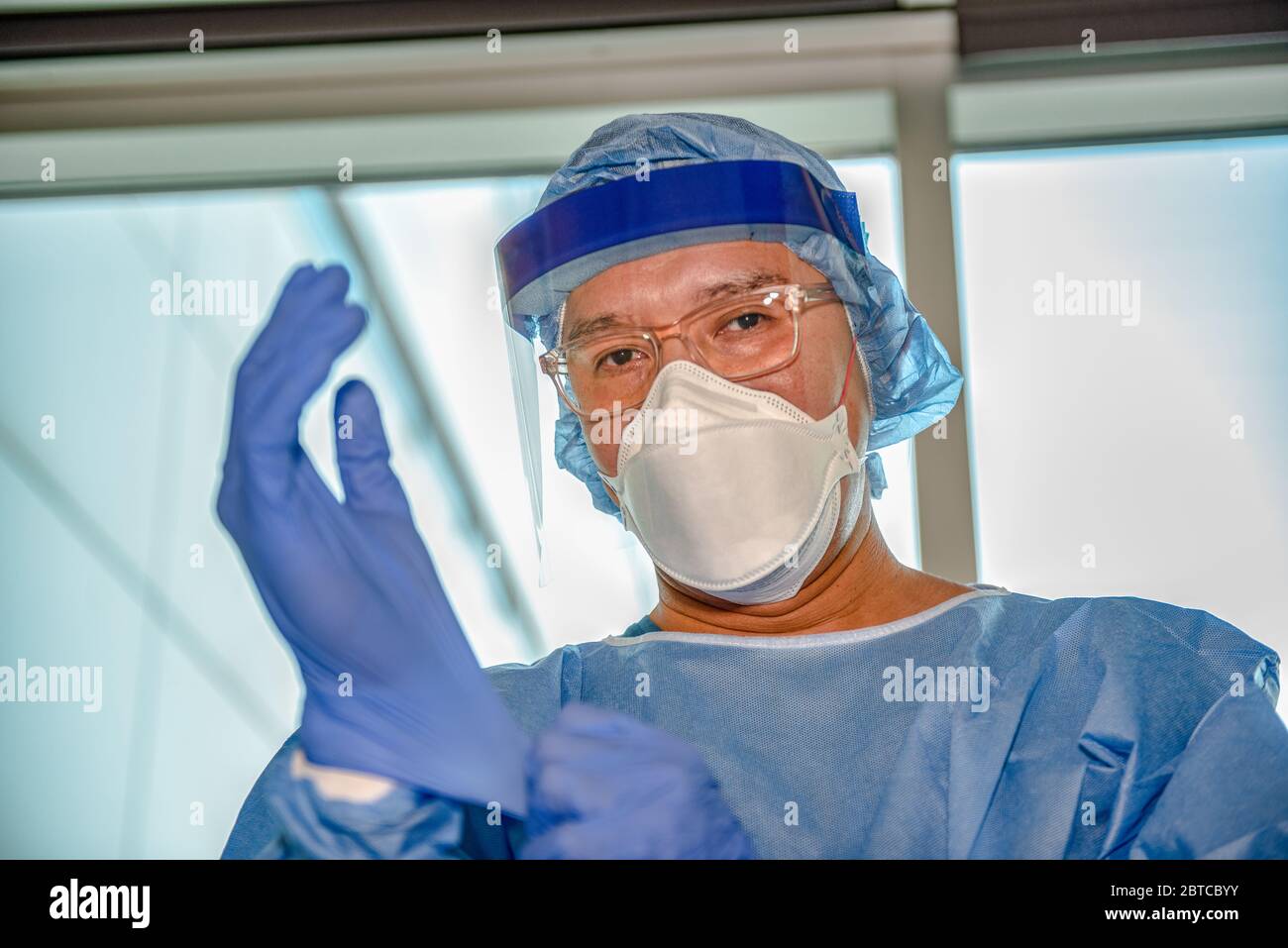 Un uomo che indossa guanti davanti a una finestra in un ospedale che si prepara a trattare un paziente con un virus contagioso trasportato dall'aria. Foto Stock