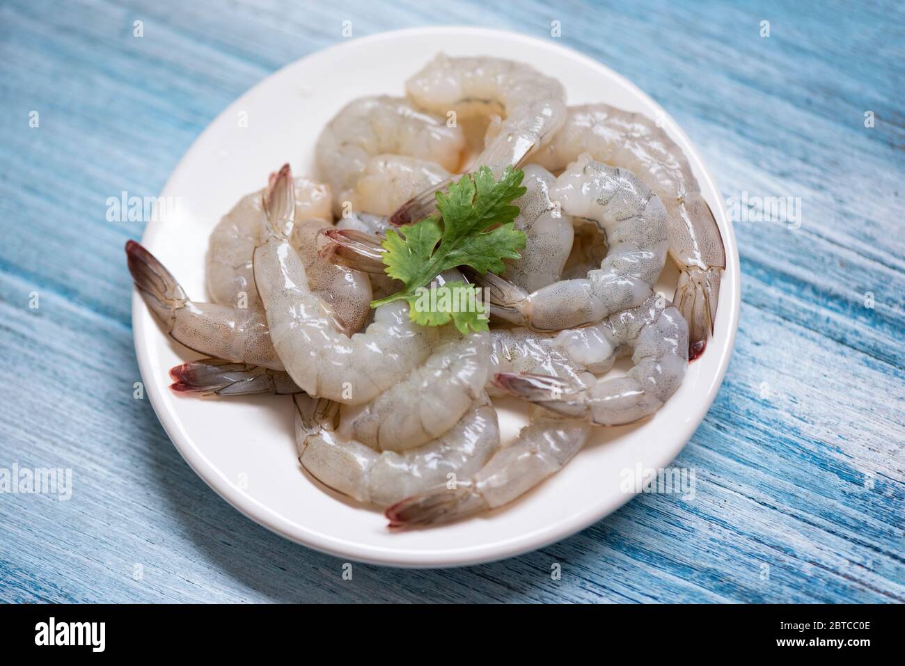 Gamberi freschi o gamberi, pesce al riparo / gamberetti crudi su piatto bianco e sfondo di legno per cucinare Foto Stock