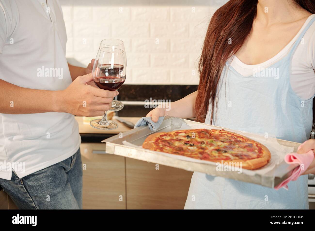 Giovane donna che tiene vassoio con pizza fatta in casa quando suo marito  porta bicchieri di vino rosso Foto stock - Alamy