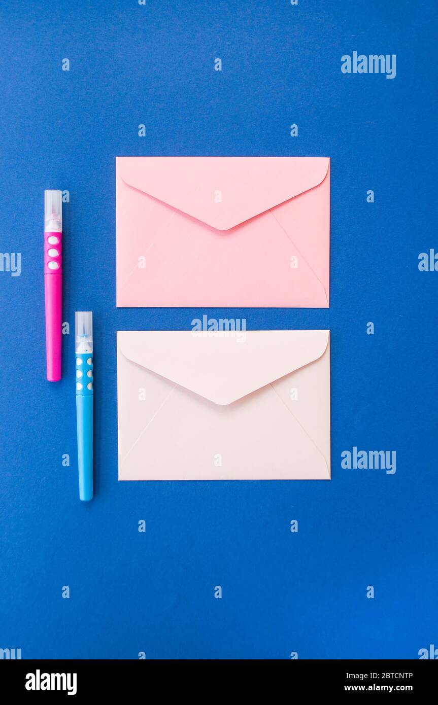 Due buste di carta rosa e bianca e pennarelli su sfondo blu classico con copyspace. Foto Stock