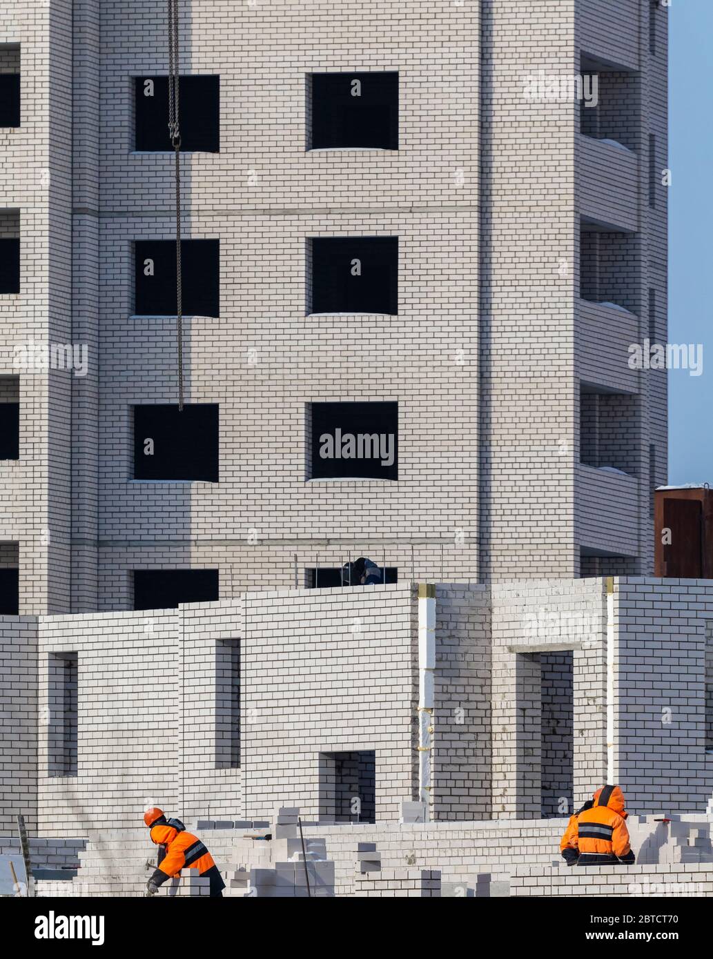 Cantiere. Edificio di appartamenti incompiuto. Operai di costruzione vestiti in mattoni di posa di abbigliamento speciale. Foto Stock