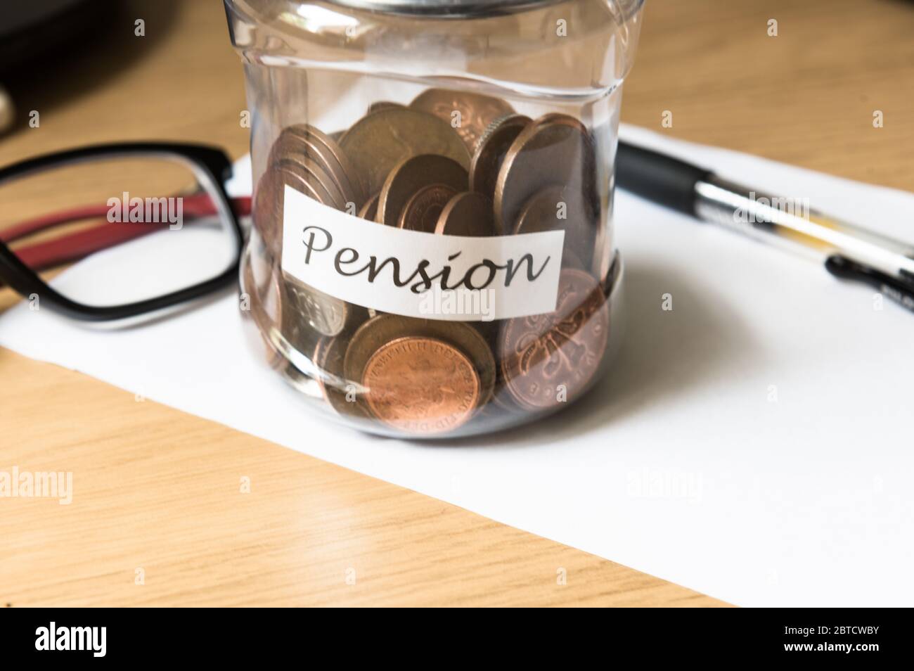 Risparmio di moneta in un vaso come banca piggy verso pensione su un tavolo con penna di carta e bicchieri Foto Stock