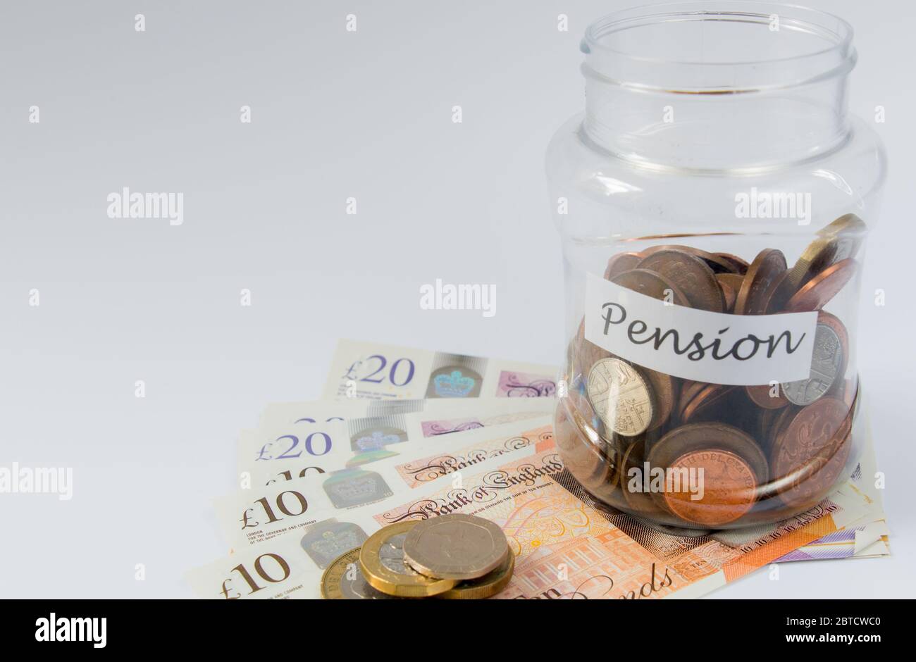 Moneta britannica e monete gettate sul tavolo in un vaso etichettato pensione verso il risparmio pensionistico Foto Stock