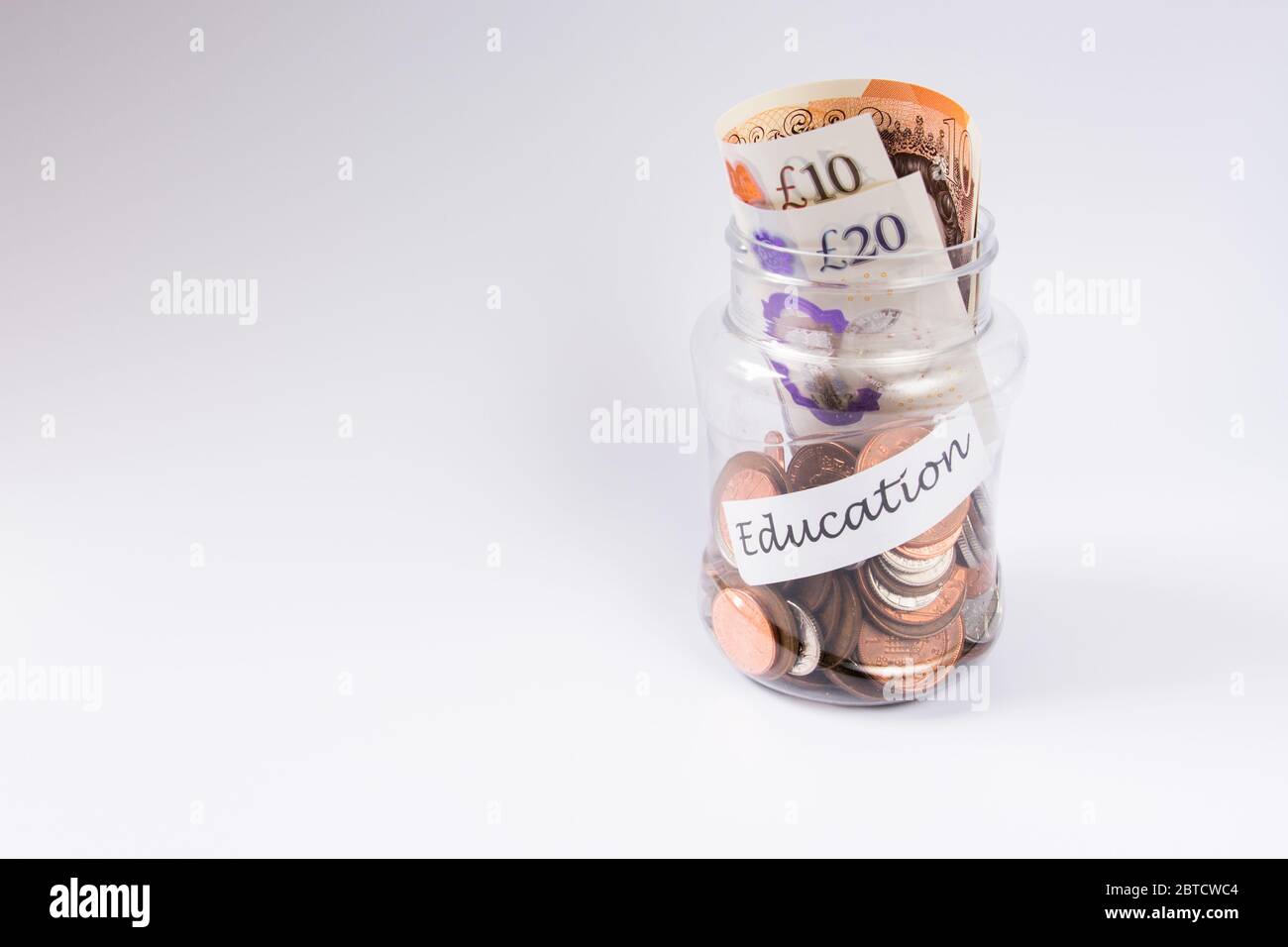 Valuta britannica e penny su vaso trasparente etichettato come Educazione su sfondo bianco Foto Stock