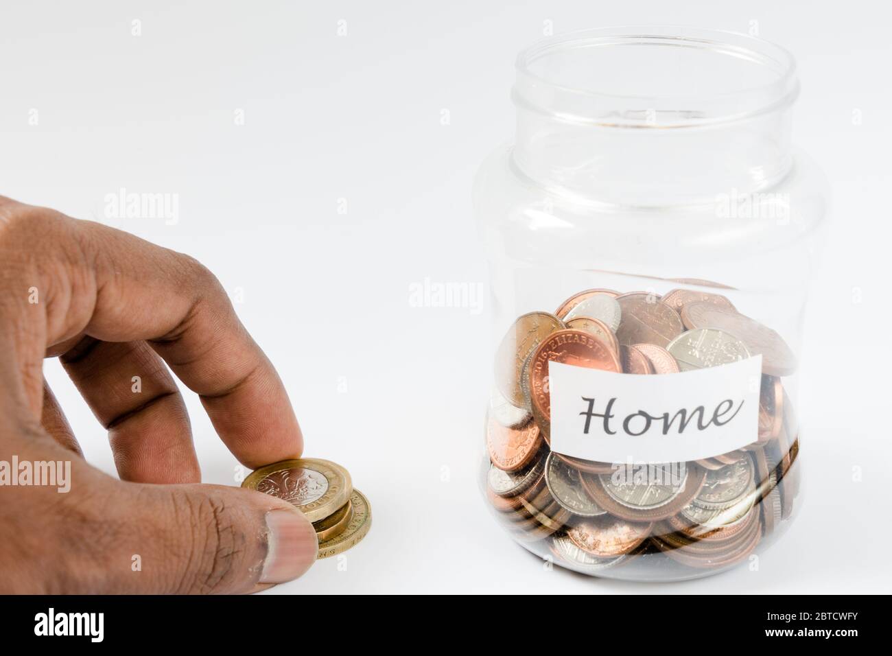 Dita che raccolgono moneta accanto al vaso di deposito domestico per aggiungere o rimuovere denaro Foto Stock