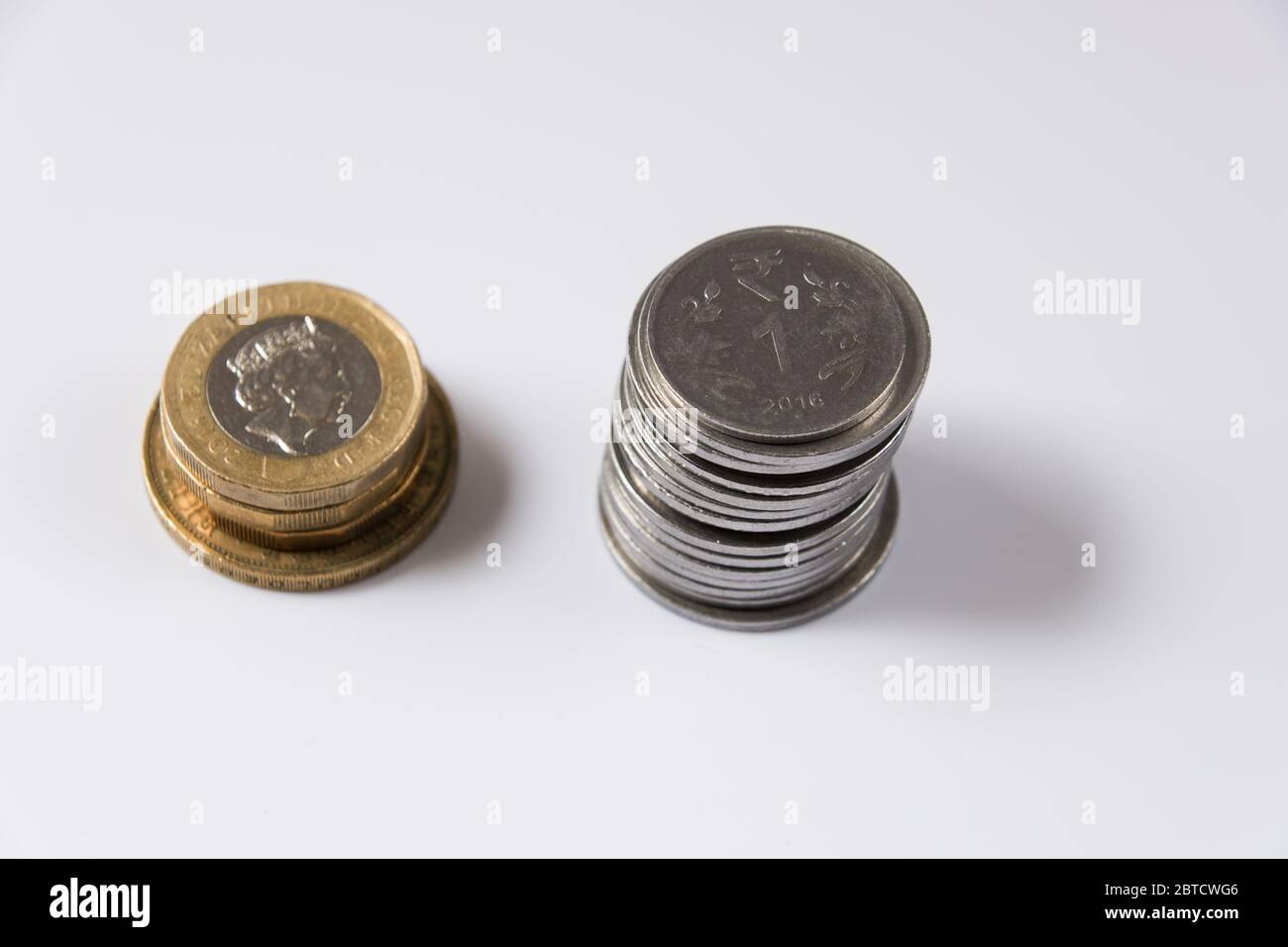 Monete inglesi e rupia indiana accatastate su sfondo bianco Foto Stock