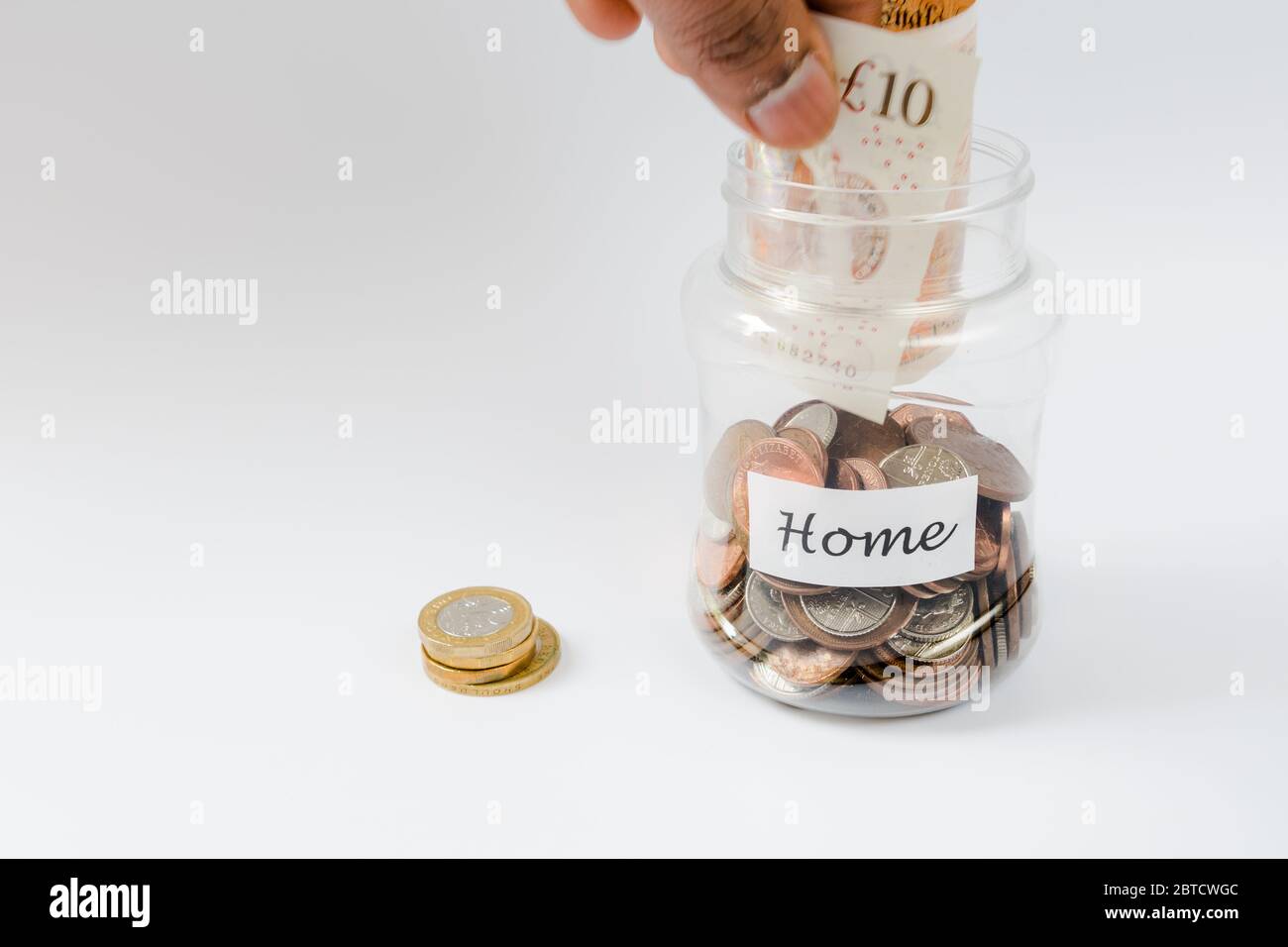 Mano che rilascia la nota di valuta nel vasetto di risparmio dei penny verso il risparmio del deposito domestico Foto Stock