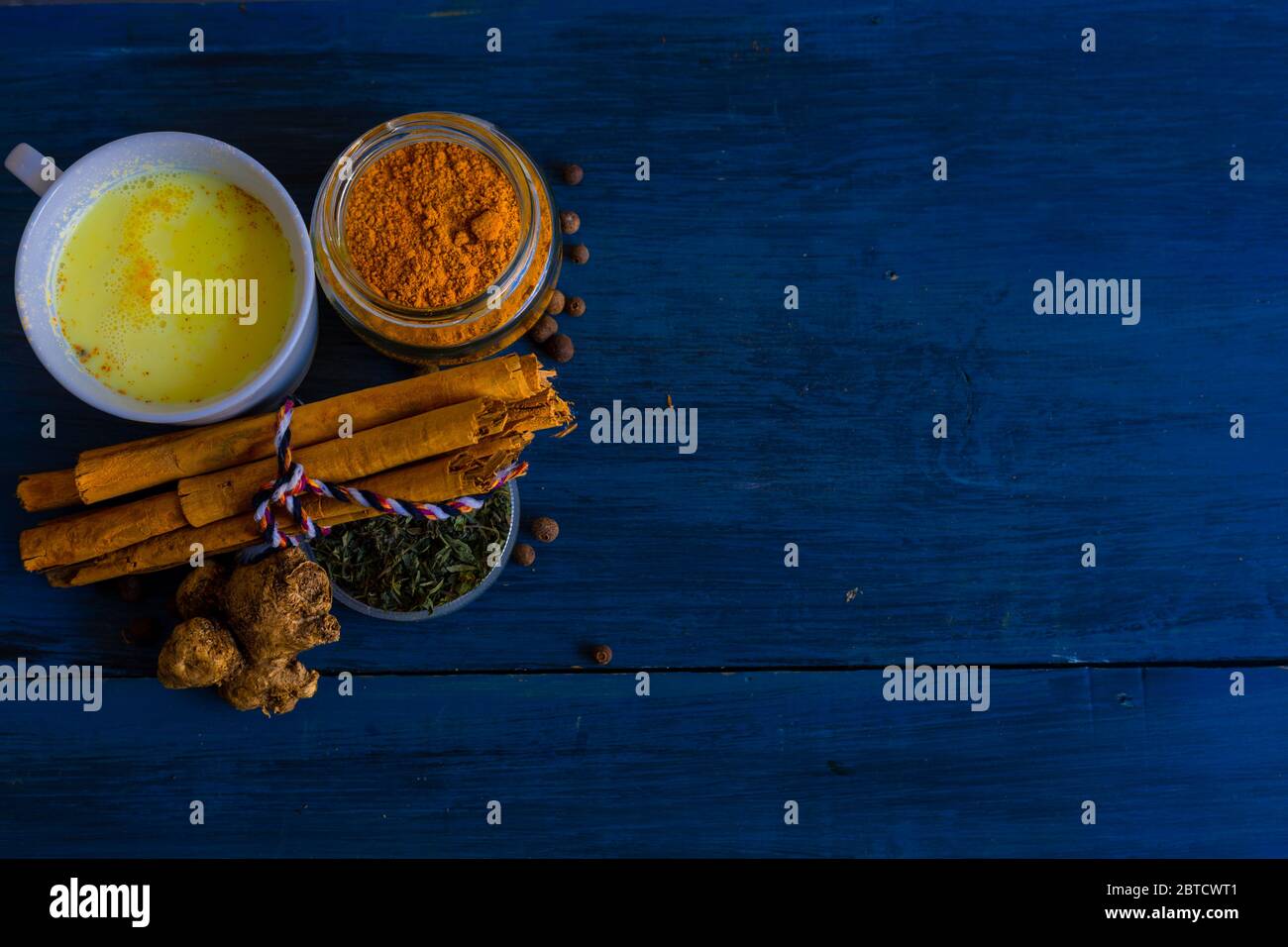 Latte in polvere dorato e un bicchiere di latte dorato, su un tavolo blu. Foto Stock