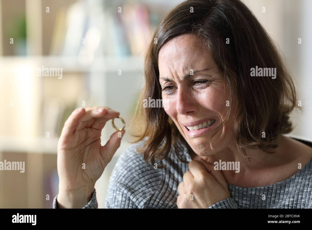 Triste moglie adulta che piange lamentandosi guardando l'anello di nozze seduto a casa Foto Stock