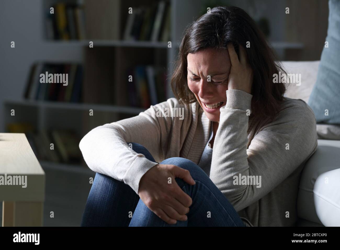 Triste donna di mezza età che piange seduto sul pavimento nel salotto di notte a casa Foto Stock