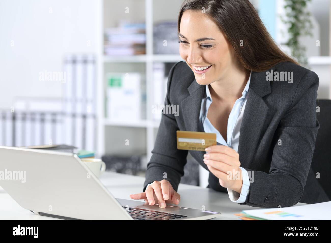 Donna dirigente felice paga online con carta di credito su computer portatile seduto su una scrivania in ufficio Foto Stock