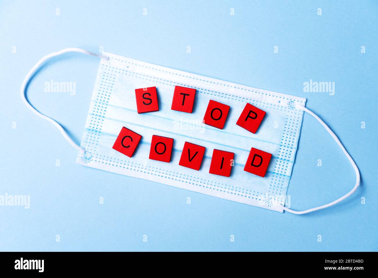 Maschera medica protettiva su sfondo blu e scritta scritta Stop Covid. Maschera facciale monouso. Protezione. Covid-19 pandemia. Rimani a casa. Sicurezza. maschera chirurgica con supporto per l'orecchio a 3 strati. Foto Stock
